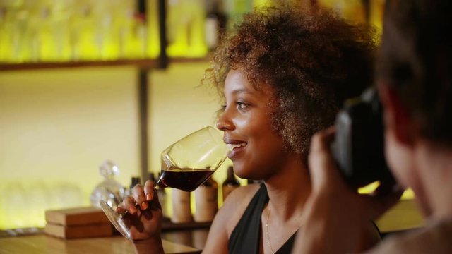 Beautiful black woman on photo session in bar. She drink wine and laughs