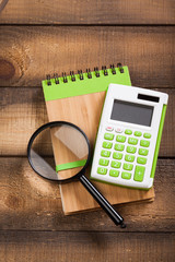 notebook on a brown wooden background with a calculator and magnifying glass