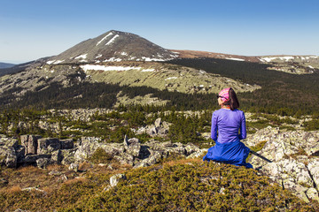 A young woman sitting on a rocky outcrop in the mountains