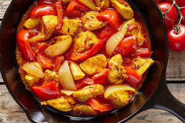 Jalfrezi chicken traditional Indian culture spicy meat and vegetables healthy food dish in cast iron pan on vintage wooden table background. Top view