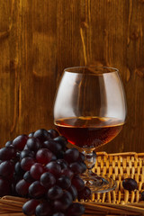 a glass of brandy and a bunch of grapes on a wicker table on the wooden background