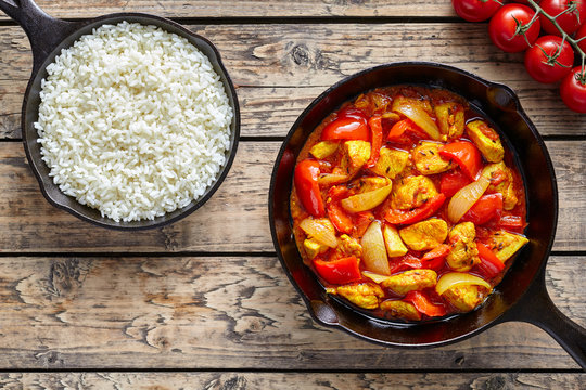 Chicken jalfrezi dietetic traditional Indian curry spicy fried meat with vegetables and basmati rice food in cast iron pan on vintage table background