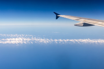 Wing of airplane flying above the clouds in the sky