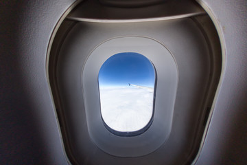 airplane window with wing and cloudy sky behind.