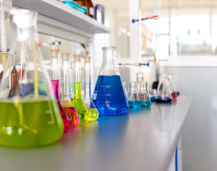 Laboratory table piled tubes with colored liquid, colored reagents in flasks and test tubes