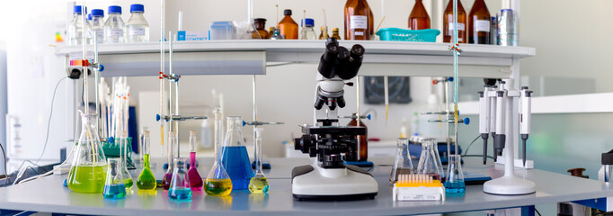 Laboratory table piled tubes with colored liquid, colored reagents in flasks and test tubes