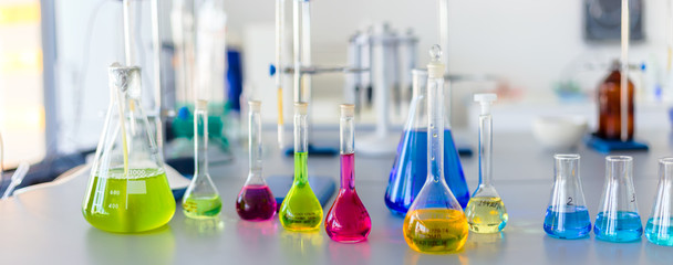 Laboratory table piled tubes with colored liquid, colored reagents in flasks and test tubes
