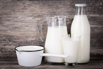 Milch in Krug, Flasche, Stieltopf und Glas auf Holz Hintergrund.
