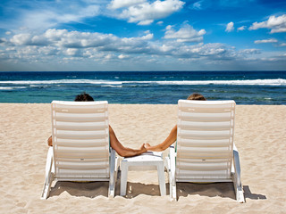 Couple in beach chairs holding hands near ocean