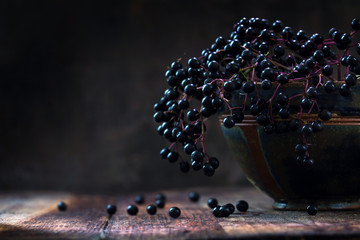 Black elderberries bunch (Sambucus nigra) in an old clay bowl, rustic wood, dark background