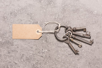 Vintage key set with blank paper tag on stone table. Symbol of new home, security and access.