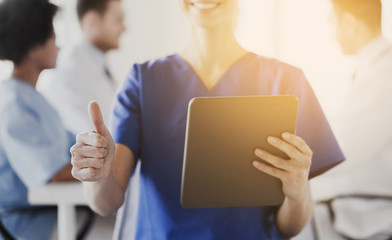 close up of nurse with tablet pc showing thumbs 
