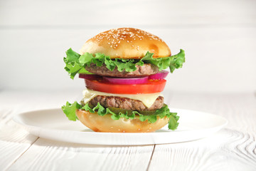 Big juicy traditional American burger with grilled meat and slices fresh vegetables closeup on a white plate on a wooden table. Food and beverages. Selective focus with shallow depth of field