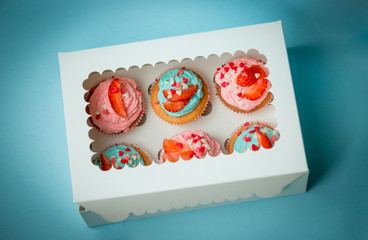 Closeup of colorful cupcakes with strawberry in paper box over b