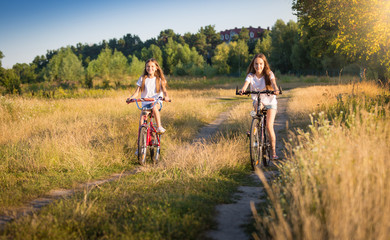 Fototapeta premium Two girls riding bicycles on meadow at sunny day