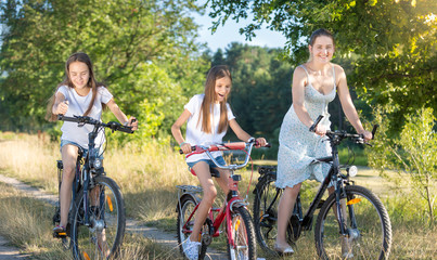 Beautiful mother cycling with two daughters at meadow