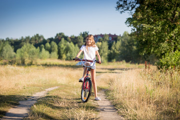 Cheerful girl riding bike in meadow at sunny day