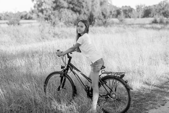 Black and white image of teenage girl riding bicycle at meadow