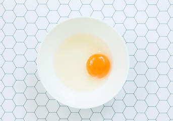 Top view of raw egg in white bowl on hexagon pattern  background.