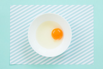 Top view of raw egg in white bowl on pattern  background.
