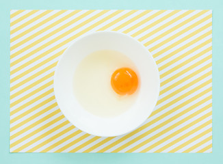 Top view of raw egg in white bowl on pattern  background.