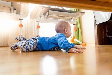 View from under the bed on baby crawling on floor at bedroom
