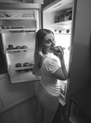 Black and white photo of hungry woman biting apple at night on k