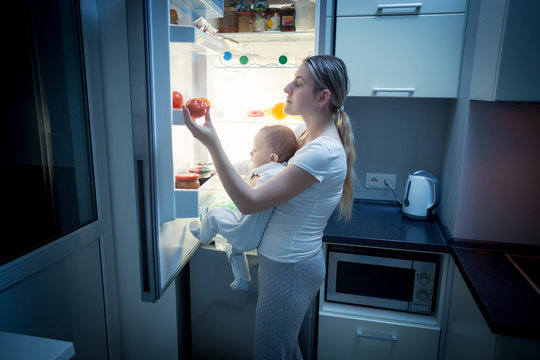 Young Mother And Baby Son Looking Inside The Fridge For Somethin