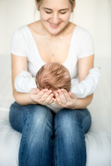 Mother sitting on bed and holding head of her 3 months old baby