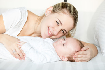 Portrait of smiling mother lying with 3 months old baby on bed