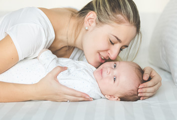 Closeup portrait of happy mother kissing her baby boy on bed