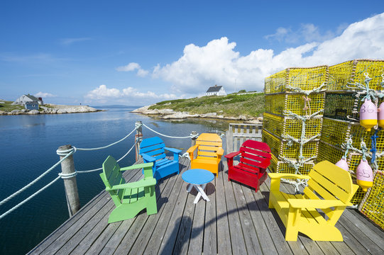 Brightly Colored Adirondack Chairs Sit Next To Stacks Of Lobster Traps On A Deck On The Shore Of A Fishing Village In Peggy's Cove, In Halifax, Nova Scotia, Canada