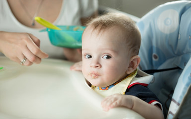 Fototapeta premium Portrait of cute baby boy sitting in highchair and looking at ca