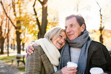 Beautiful senior couple hugging in park, drinking coffee. Autumn