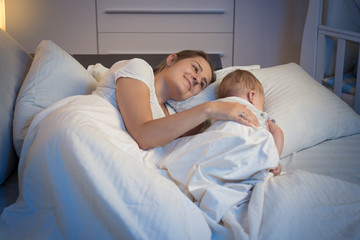 Night shot of smiling mother lying on bed with her beautiful bab