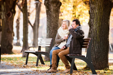 Fototapeta premium Senior couple sitting on bench, drinking coffee. Autumn nature.