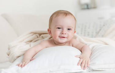 Cheerful smiling baby boy lying on big bed