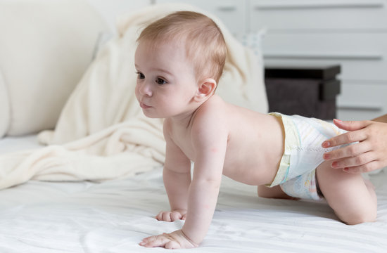 9 months old baby boy in diapers crawling on bed with white shee
