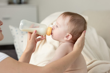 Closeup of mother giving milk from bottle to her baby son sittin