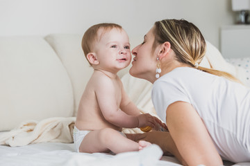 Fototapeta na wymiar Beautiful young mother kissing baby boy in cheek on bed