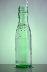 Green bottle with clean drinking water on the table. Bubbles in the glass transparent bottle.