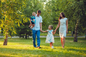Naklejka na ściany i meble Happy young family of four people walking and having fun in the park
