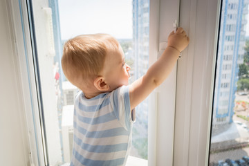 Baby in danger. Little baby trying to open window and pulling by