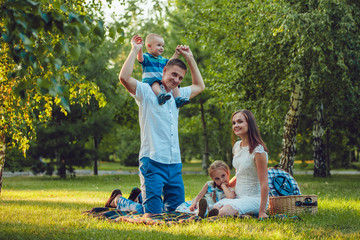 Fototapeta premium Young happy family of four on picnic in the park and father holding his son on shoulders