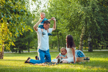 Young happy family of four on picnic in the park and father holding his son  shoulders