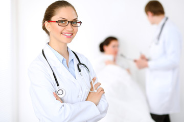 Cheerful smiling female doctor on the background with physician and his patient in the bed. High...