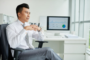 Asian entrepreneur sitting in chair and looking through window