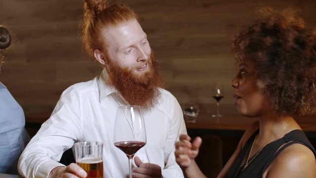 Hipster with a ginger beard flirts with a very beautiful black woman in a luxury bar. He buy her a drink