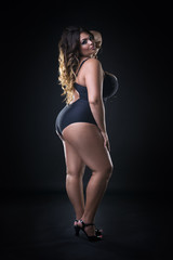 Young beautiful caucasian plus size model in swimsuit, xxl woman on black background