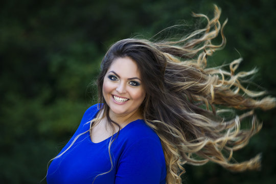 Young beautiful caucasian plus size model in blue dress outdoors, xxl woman on nature with developing in the wind hair